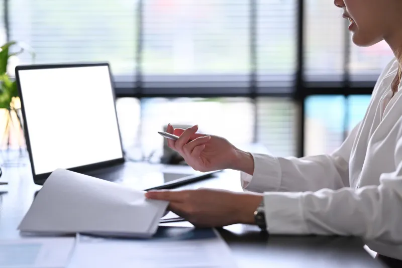 Hands working on paperwork at a laptop